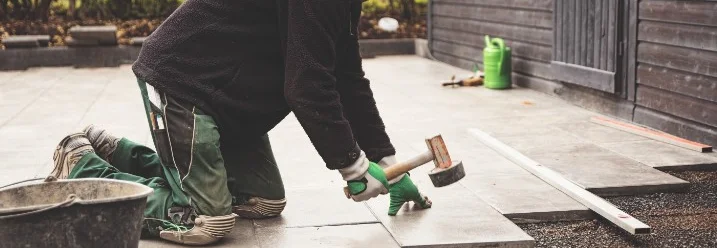 Person verlegt Terrassenplatten mit Gummihammer